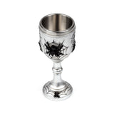 Angled view of a decorative, silver-coloured goblet. It features raised black spiders and intricate spider web patterns on its textured exterior, with a polished metallic inner cup.