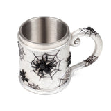 Angled view of a decorative spider web tankard with a textured white body, black spiders, a metallic silver interior, and an ornate handle.