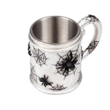 Angled view of a decorative tankard, featuring a textured silver-coloured exterior with black spider web patterns and raised black spiders, and a smooth metallic interior.