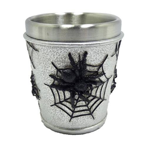 Angled view of a decorative shot glass featuring a brushed silver-coloured rim and a stippled light grey body. A raised black spider sits on an intricately detailed black web, with other web designs visible around the sides.