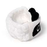 Elevated angled view of a white plush panda headband with black ears and eye patches.