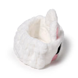 Angled view of a white plush rabbit headband with pink inner ears, black embroidered eyes, and pink nose on a white background.