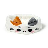 Front view of a white plush cat headband with orange and grey ears, black embroidered eyes, pink nose, and pink cheeks.