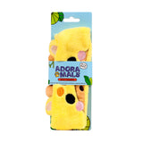 Front view of a yellow plush beauty headband with giraffe ears, small horns, and brown spots, packaged on light blue card with tropical leaves.
