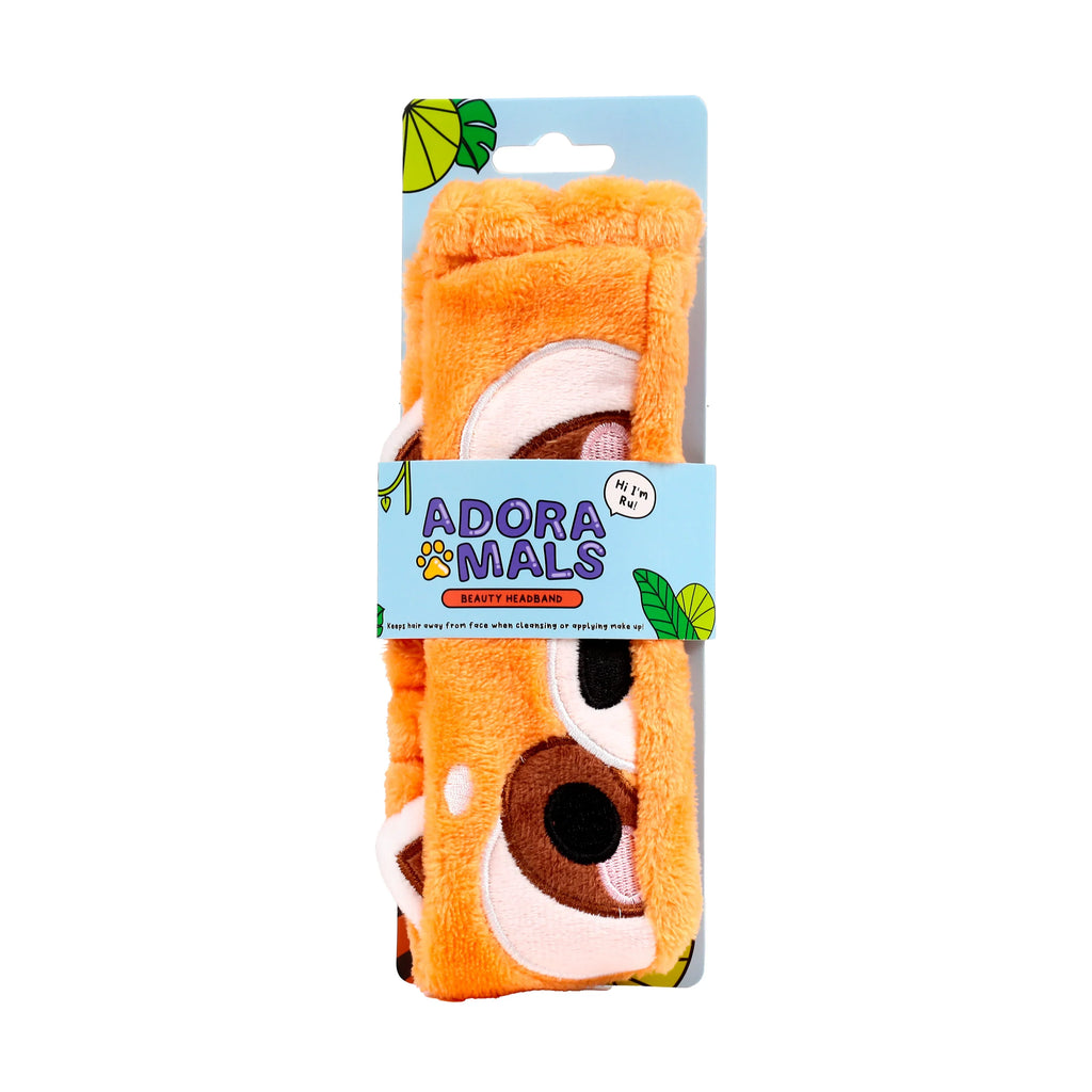 Front view of an orange plush beauty headband, featuring a red panda character design with stitched white, brown, and black facial details, presented on a light blue backing card.