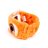 Orange plush beauty headband, designed as a red panda, with embroidered eyes, nose, and inner ears visible from an overhead, angled view.
