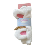 Front view of a white plush unicorn beauty headband with pink inner ears and a golden horn, presented on retail packaging.