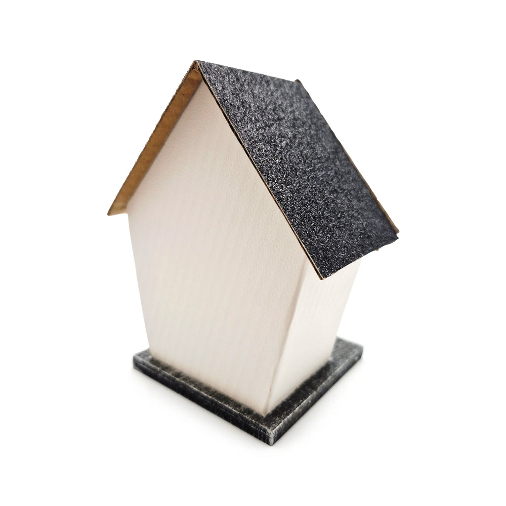 Angled view of a small house decoration with smooth, light-coloured walls, a dark, glittery gabled roof, and a dark base, on a white background.