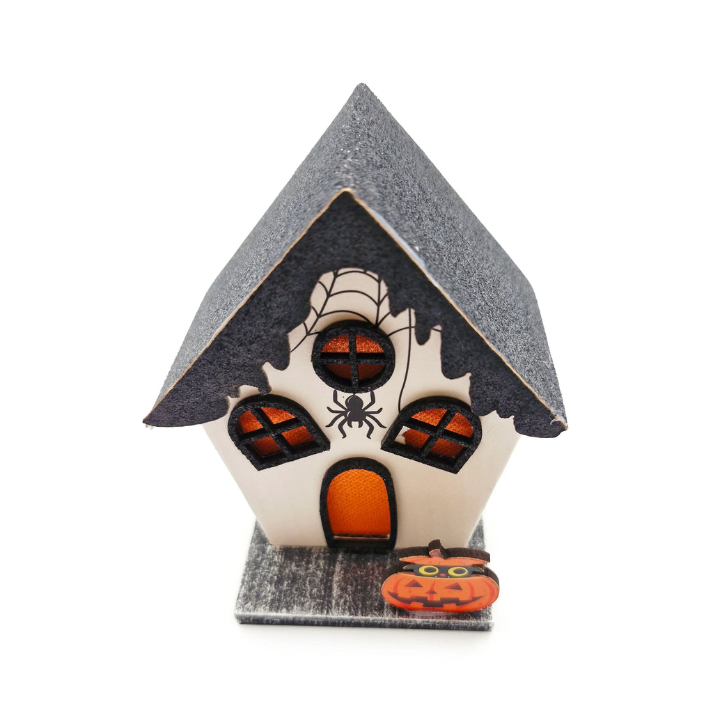 Angled view of an LED Halloween spooky house decoration featuring a dark glittery roof, cream-coloured walls, dripping spiderweb details, an orange glowing door and windows, and a pumpkin with a black cat at its base.