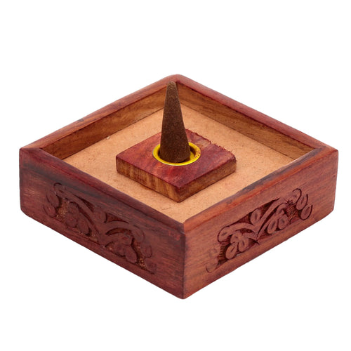 Angled view of a square Sheesham wood incense cone holder with carved floral patterns, featuring a brown pyramid incense cone held by a yellow metal insert.