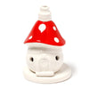 Front-angled view of a red and white ceramic fairy toadstool house incense burner. It features a glossy red mushroom cap with white spots, a white house-shaped base with two round holes and a moulded door detail, and an integrated circular base.
