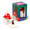 Angled view of a white ceramic toadstool house incense cone burner with a red spotted cap, shown disassembled next to its illustrative packaging box. A brown incense cone sits on the burner's white circular base.