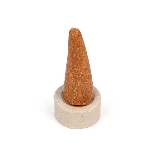 Angled view of a reddish-brown incense cone with granular texture, placed in a light grey, round ceramic holder.