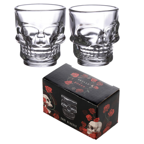 Angled view of two clear glass skull shot glasses and their black presentation box, decorated with red roses, skulls, and 'SKULLS + ROSES', 'SHOT GLASSES' text.