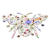 Wooden jigsaw puzzle shaped as a large bee, displaying a vibrant nectar meadows floral pattern with colourful flowers and smaller bees. Several loose, unique bee and flower-shaped wooden pieces are visible around the main bee.