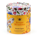Angled view of a cylindrical wooden jigsaw puzzle container. It features a white lid with colourful floral and bee patterns, and a yellow base displaying 'Nectar Meadows Wooden Jigsaw' text alongside illustrative floral and bee designs.