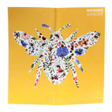 Front view of a wooden jigsaw puzzle design, depicting a large bee silhouette filled with colourful floral patterns and smaller bees against a bright yellow background. The words 'WOODEN JIGSAW' are visible at the top right.