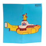 Front view of the unfolded artwork for a wooden jigsaw puzzle, featuring a cartoon illustration of The Beatles Yellow Submarine in yellow, red, blue, and white colours.