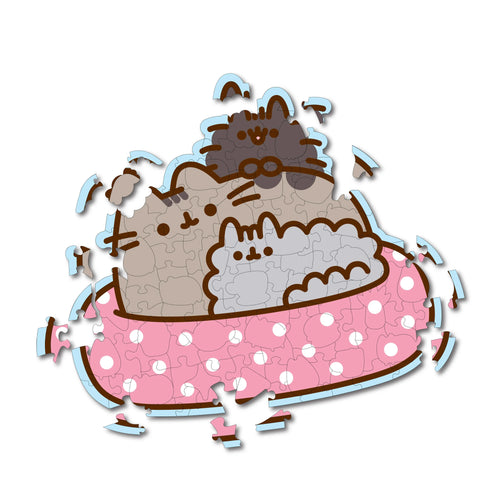 130-piece wooden jigsaw puzzle depicting three Pusheen cats, in various grey and brown tones, nestled in a pink spotted bed. The puzzle pieces are visible and partially assembled against a white background.