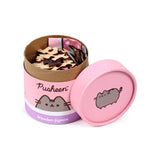Angled view of an open pink wooden jigsaw puzzle container, showing natural wood pieces inside. The container side is decorated with 'Pusheen' text and a grey cat illustration, with a matching Pusheen the Cat illustration on the pink lid.