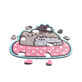Angled view of a partially assembled 130-piece wooden jigsaw puzzle, depicting Pusheen the Cat and other cats resting on a pink, polka-dotted cushion, with several loose pieces scattered on a white background.