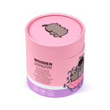 Angled view of pink cylindrical packaging for a wooden jigsaw puzzle, depicting a Pusheen cat graphic on the lid and side, with WOODEN JIGSAW and 130 pieces text.