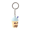 Front view of a 3D PVC bubble tea keyring featuring a light yellow cup with brown boba pearls, a light blue domed lid, a purple straw, and a cute smiling face with black eyes and pink cheeks, attached to a silver-coloured metal chain and split ring.