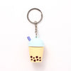 Front view of a 3D PVC bubble tea cup keyring, featuring a pale yellow base, dark brown boba pearls, light blue domed lid, purple straw, and silver-coloured metal ring with chain.