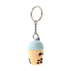 Front view of a 3D PVC Boba bubble tea cup keyring, featuring a light yellow cup, light blue lid, purple straw, cartoon eyes with pink blush, and brown boba details.