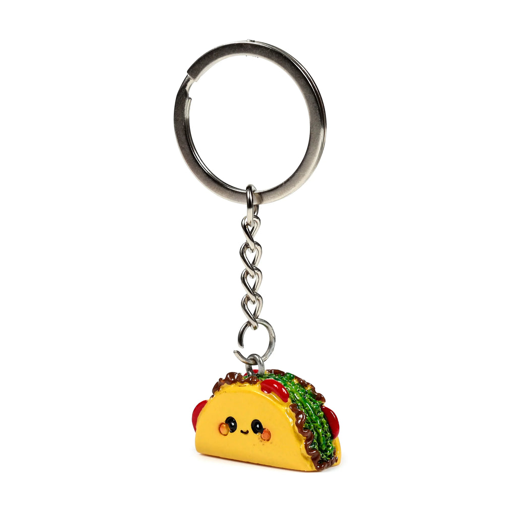 Front view of a novelty taco keyring, featuring a yellow taco charm with a cute smiling face and colourful green and red fillings, suspended from a silver-coloured split key ring.