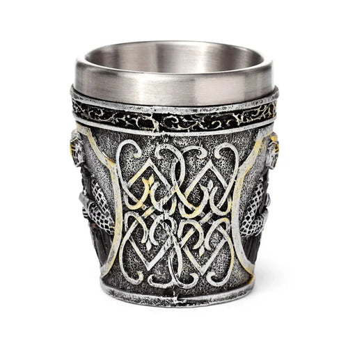Decorative medieval shot glass, angled view showing intricate silver and faded gold Celtic knotwork patterns on an antiqued silver-grey exterior. Features sculpted side details and a smooth metallic interior.