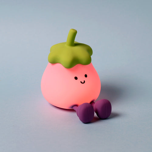 Angled view of a glowing pink sleep lamp night light character, with a lime green top and purple feet, featuring a black smiling face, sitting on a light blue background.