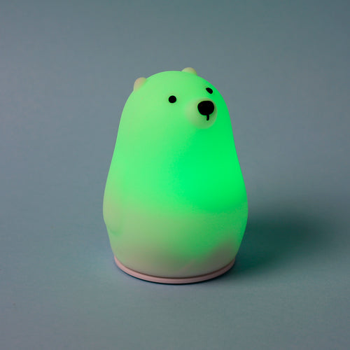 Angled view of an Adoramals polar bear sleep lamp, glowing green, with black eyes and nose, on a pale grey background.