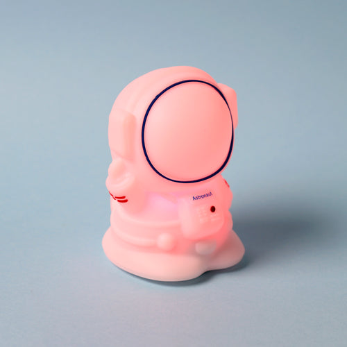 Angled view of an astronaut night light glowing pink, featuring a blue visor outline and 'Astronaut' text on its chest, set against a light blue background.