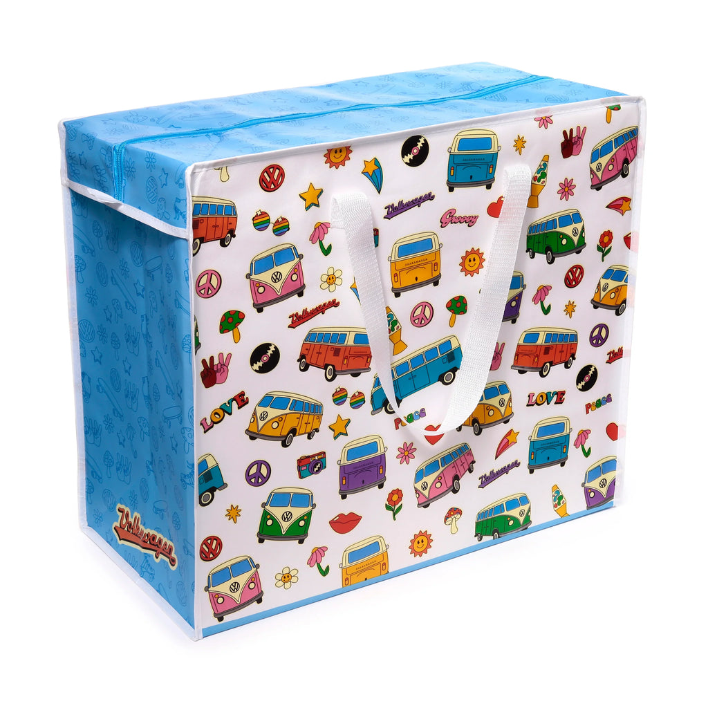 Angled view of a colourful laundry and storage bag, featuring retro Volkswagen T1 camper bus illustrations, peace signs, flowers, and 'Love', 'Peace', 'Groovy' lettering on a white background, with a blue zip-up top and white fabric handles.