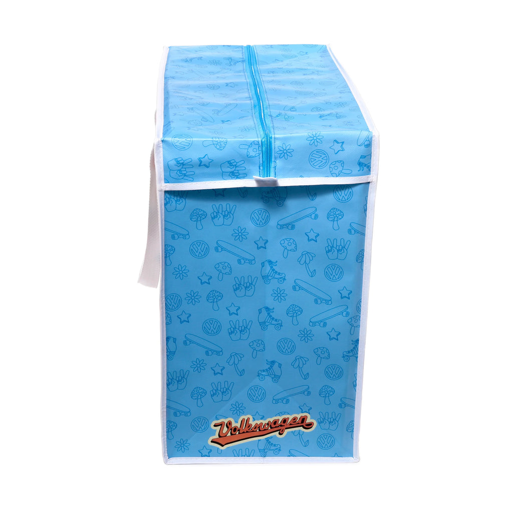 Angled view of a light blue laundry and storage bag with a white zipper. The bag features a retro pattern of darker blue outlines including VW logos, peace signs, mushrooms, skateboards, roller skates, flowers, and stars. A large orange and cream Volkswagen script logo is visible on the lower front, and a white strap is on the side.