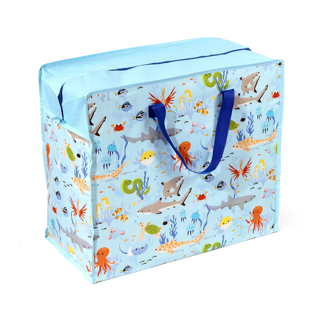 Angled view of a light blue Mariniverse laundry and storage bag, featuring a colourful sea creature pattern with sharks, octopuses, jellyfish, and fish. The bag has dark blue handles and a zippered light blue top.
