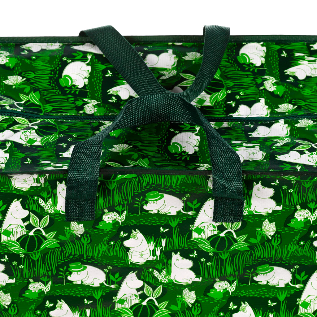 Close-up of a green Moomin Garden Life laundry and storage bag, showing its top with tied dark green fabric handles and a zip closure. The bag features a pattern of white Moomin characters, green foliage, and butterflies.