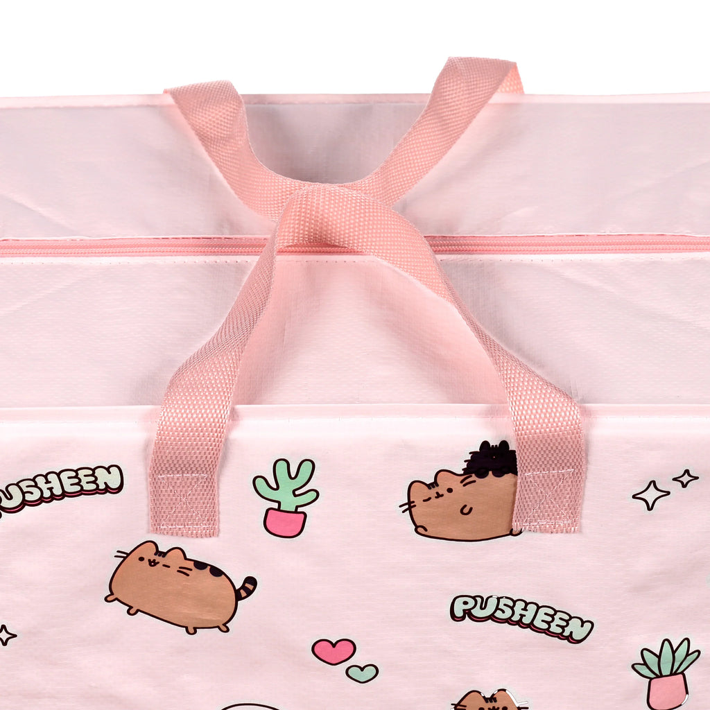 Close-up, angled view of a pink laundry and storage bag, featuring a pattern of Pusheen the Cat and various plants. The image shows the pink fabric handles and a matching pink zip closure at the top.