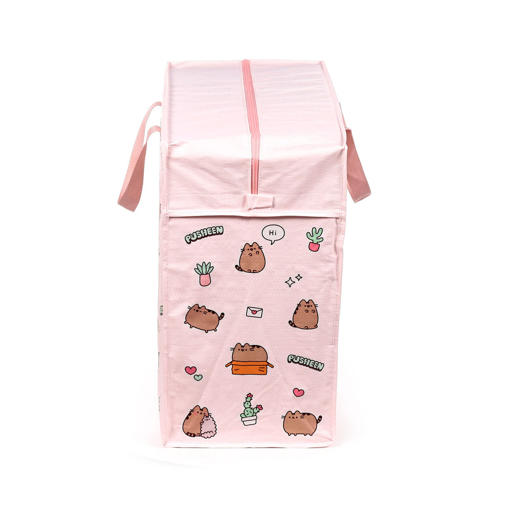 Front view of a pink laundry and storage bag, standing upright, with a design featuring cartoon Pusheen cats, potted cacti, hearts, and stars. It has a pink zip closure at the top and fabric handles.