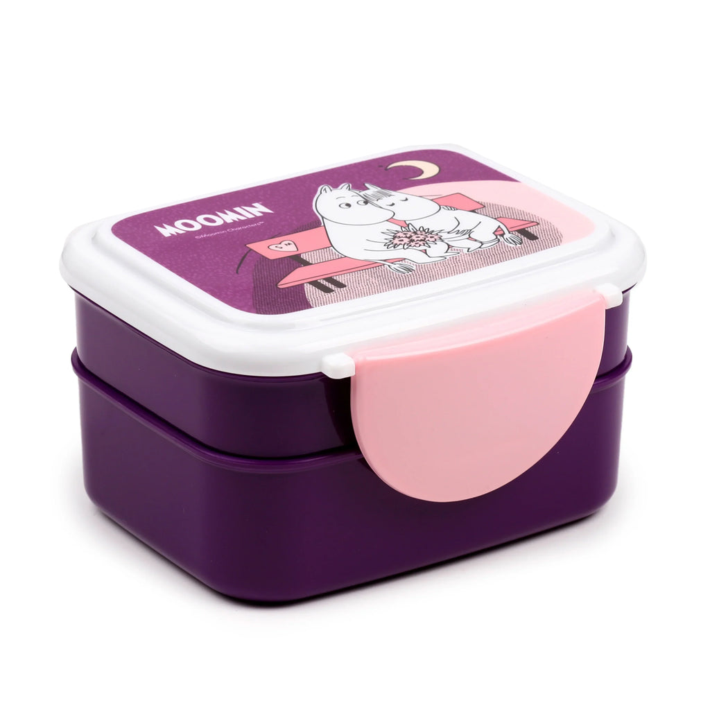 Angled view of a two-tiered purple bento lunch box. It has a white lid featuring a purple Moomin design with two white characters sitting on a pink bench, one holding a bouquet. A pink clip lock is visible on the side.