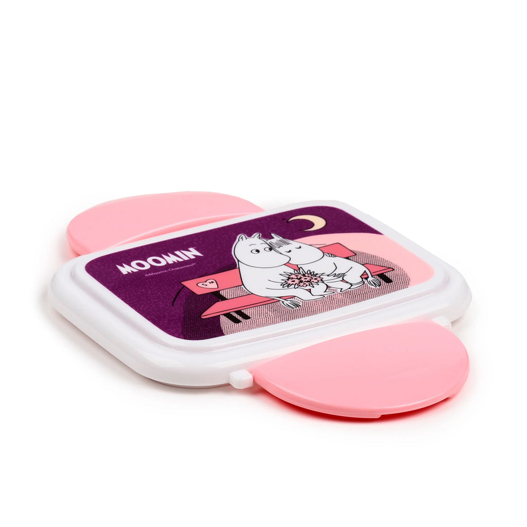 Angled view from above of a white and pink Moomin clip lock bento lunch box, depicting Moomin characters on the purple lid.