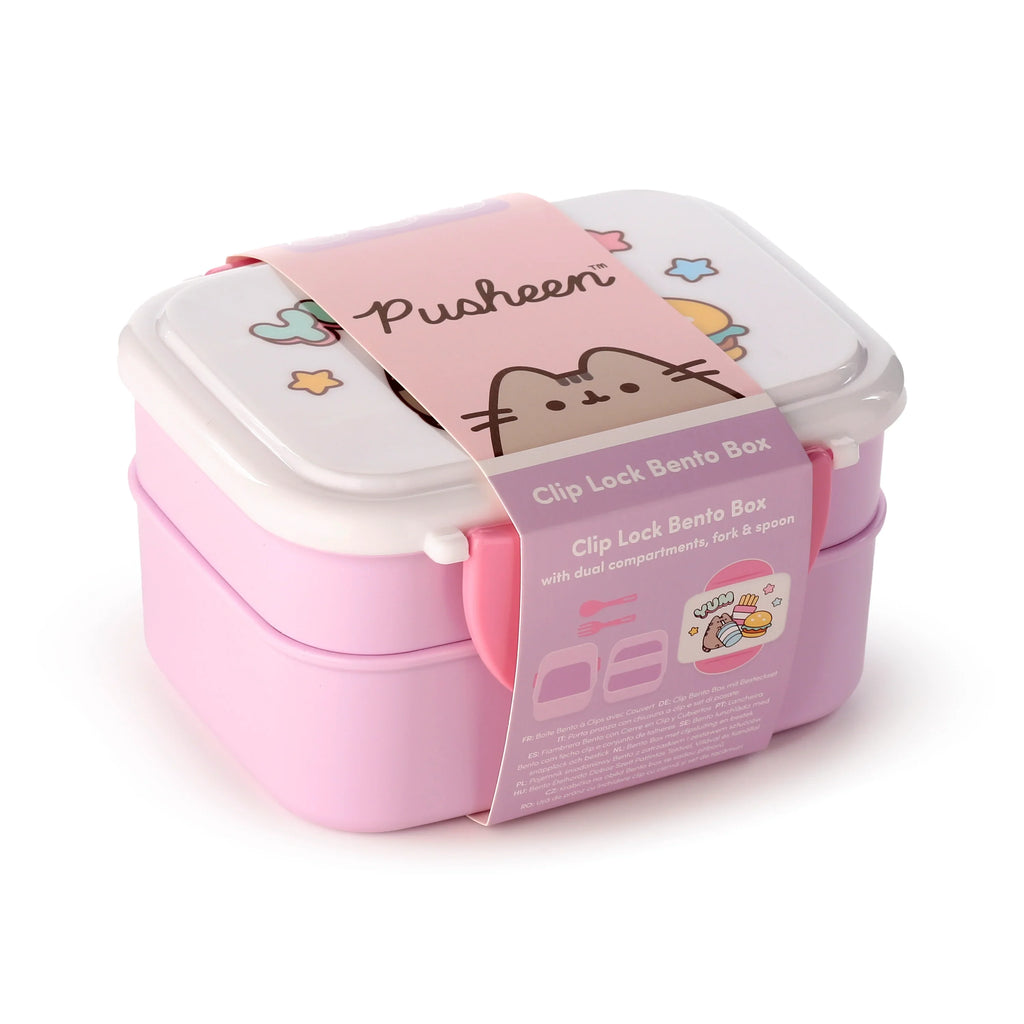 Angled view of a pink and white bento clip lock lunch box with visible side clips. A paper band, featuring a Pusheen cat illustration and icons indicating dual compartments and included cutlery, wraps around the box. The white lid displays faint outline illustrations.