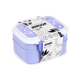 Elevated angled view of a two-tier lavender Moomin bento lunch box with white clip locks, a Moomin-patterned lid, and a decorative strap featuring Moomin character illustrations.