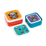 Angled view of a set of three Day of the Dead lunch boxes. The colourful lids feature intricate sugar skull designs; one large red box, one medium teal box, and the smallest box's lid displaying multiple sugar skulls placed separately.