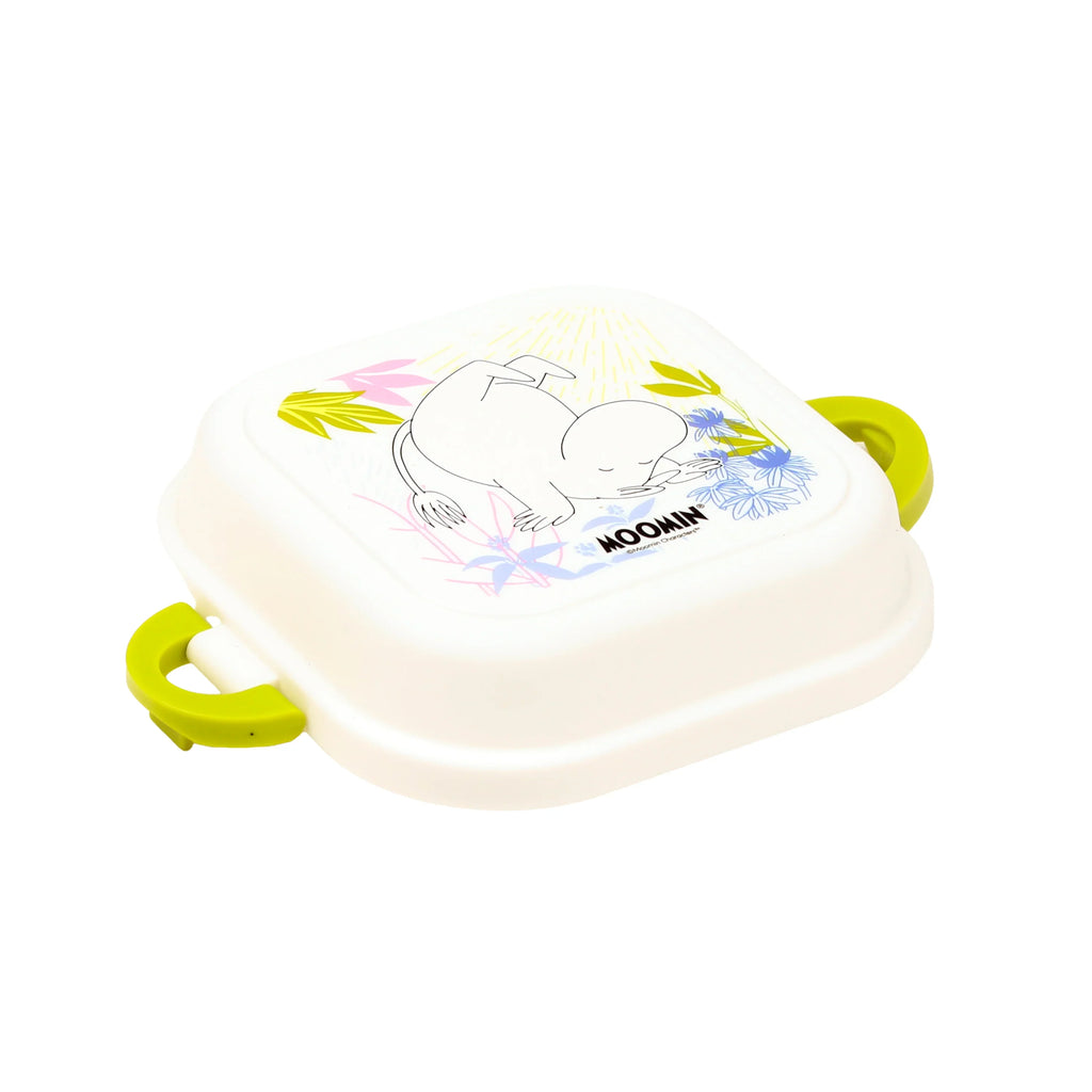 Angled view of an off-white bento clip lock snack lunch box, depicting a Moomin character lying amongst pink, blue, and green flowers on the lid, with bright lime green clips.