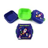 Overhead view of a disassembled deep blue and bright green Bento Clip Lock Snack Lunch Box. The blue lid, with its green side clips, features a colourful 'Space Cadets' design depicting rockets, astronauts, and planets. Visible packaging text includes 'Space Cadets' and 'CLIP LOCK Snack BOX'. The inner green compartment and separate blue base are also shown.