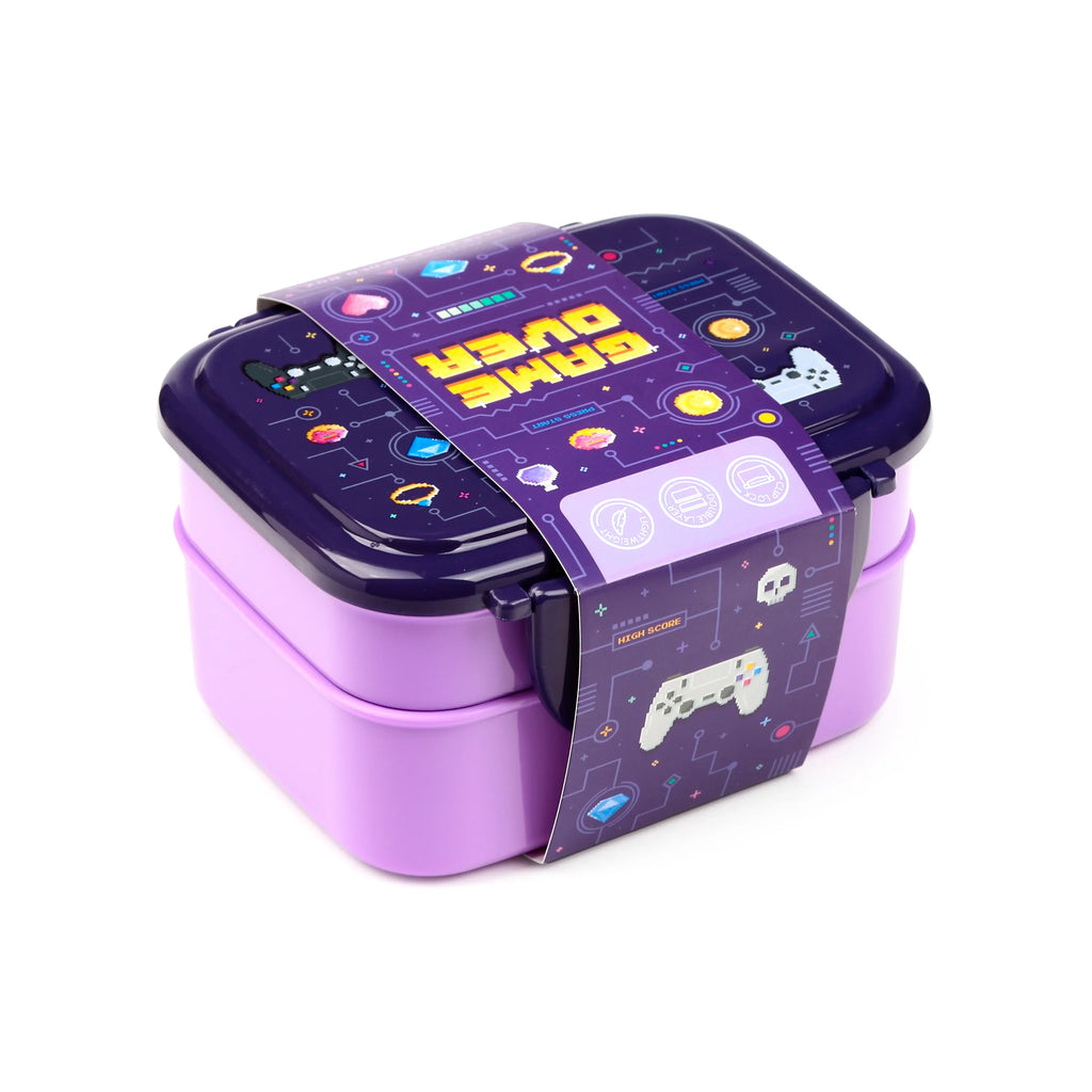 Angled view of a two-tier bento lunch box with a dark purple 'Game Over' pixelated lid, lavender base, clip locks, and a decorative band with gaming graphics.