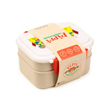Angled view of a double-layer bento clip lock lunch box, featuring a white lid with colourful Pippi Longstocking illustrations and a beige base, secured by orange side clips. A beige cardboard sleeve depicting Pippi Longstocking wraps around the box.