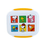 Top view of a white bento clip lock lunch box with yellow fastenings. The lid features six colourful square panels depicting Peanuts characters Snoopy and Woodstock in various poses.